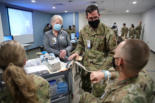 Air Force Lt. Kyle Costello, center, a registered nurse assigned to the team deployed to Lawrence General Hospital, ties restraints on Lt. Benjamin Stone, right, also a registered nurse, during a training exercise. (U.S. Army photo by Spc. Daniel Thompson) 7047579.jpg